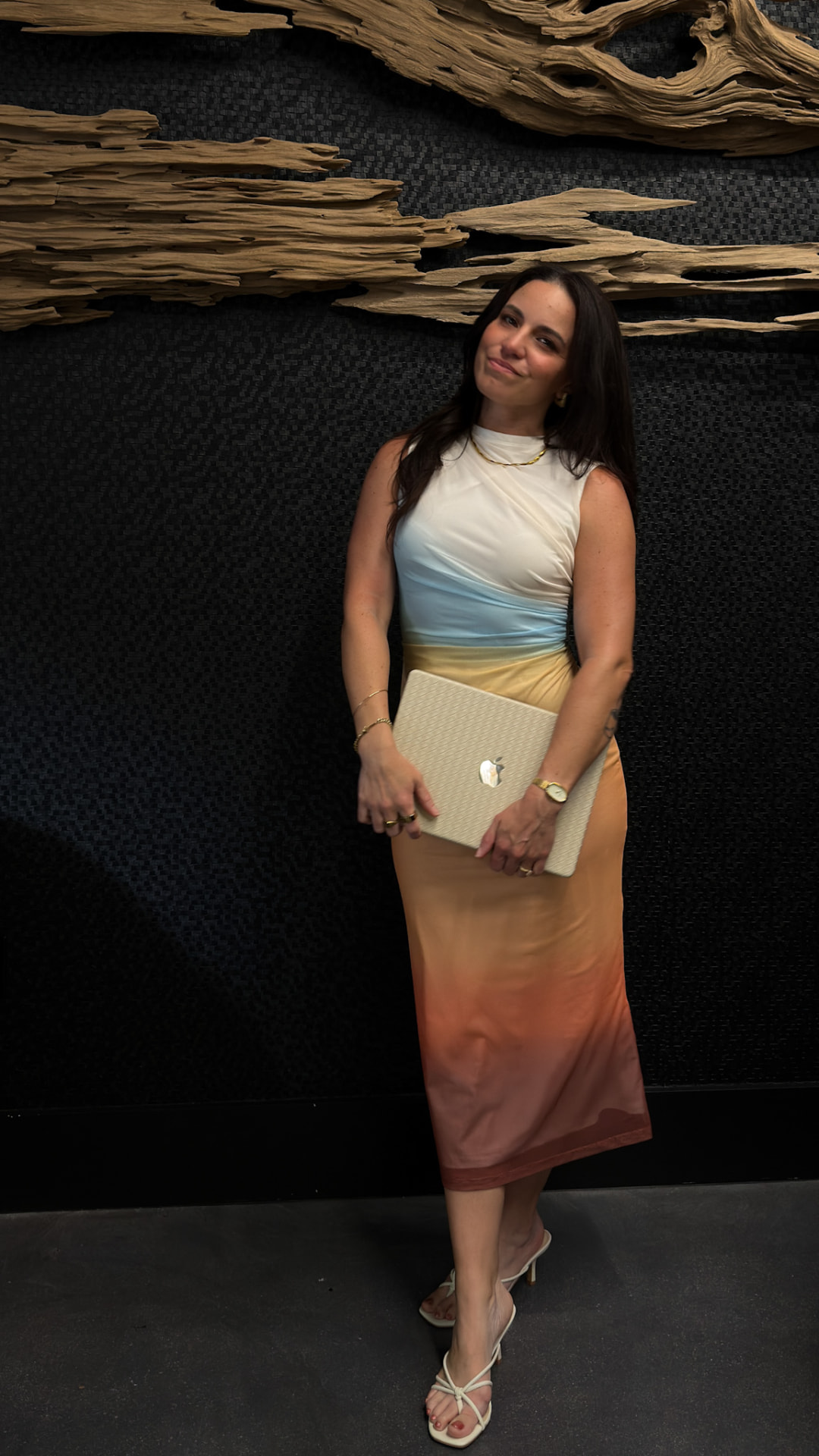 Angelica Marie standing against a dark textured wall holding a laptop